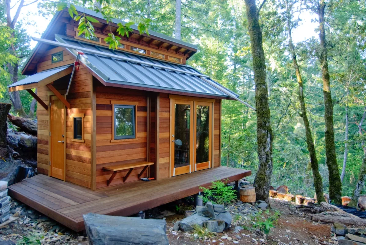 Wooden tiny cabin with deck among tall trees in the woods