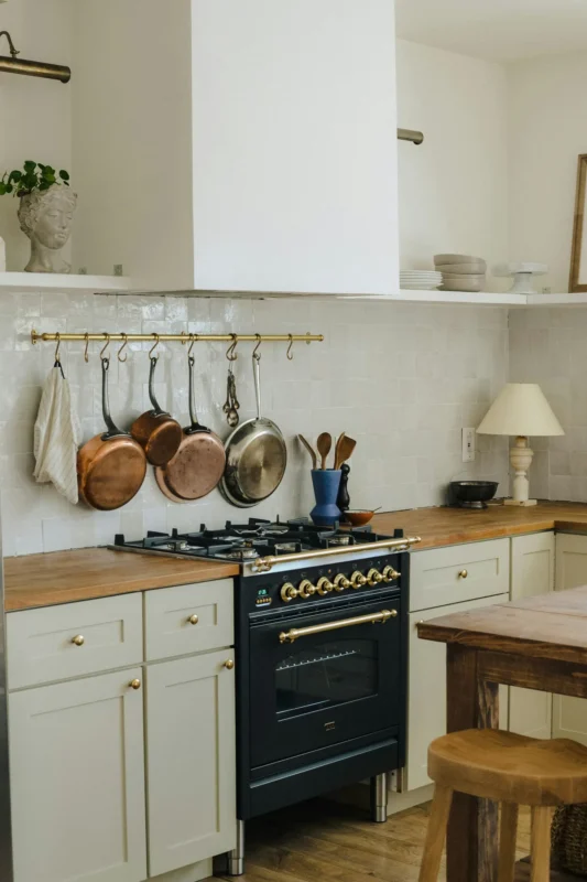 Copper pots and pans hanging from a brass wall rail above the stove