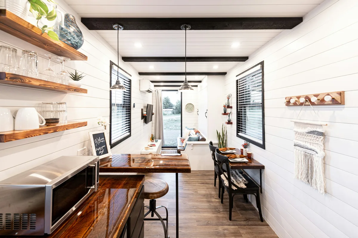 Bright tiny house interior with white shiplap walls, open wooden shelves and small dining nook