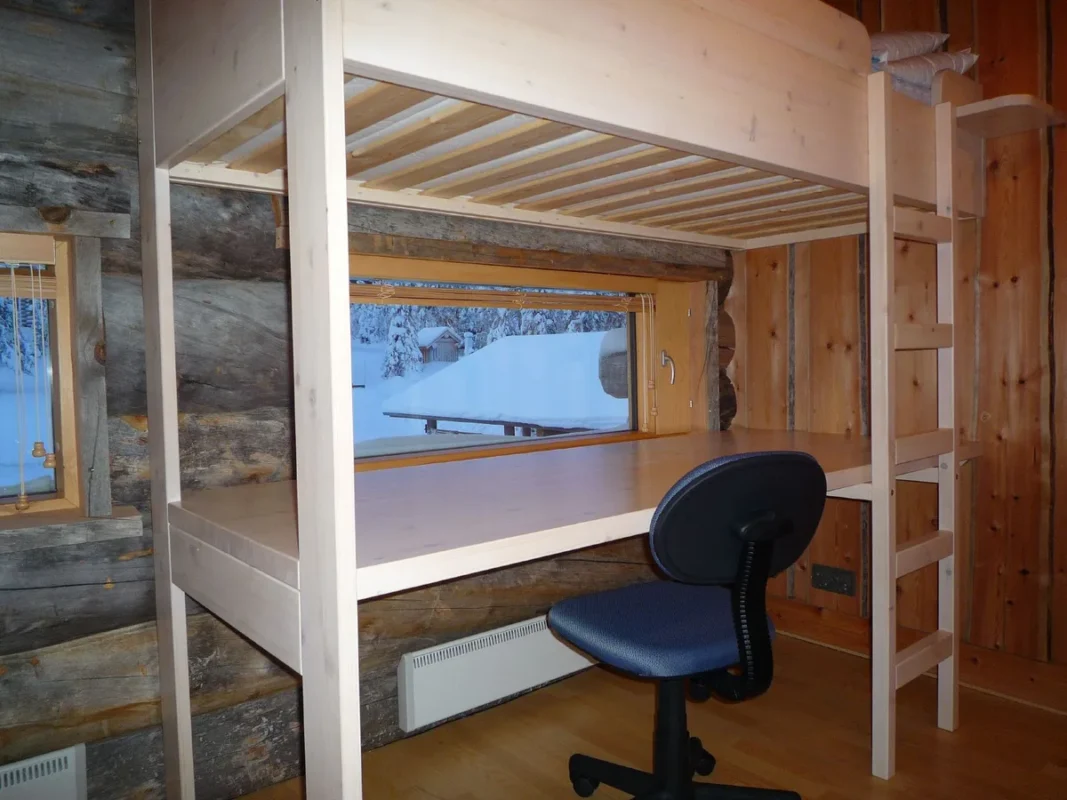 Wooden loft bed with desk and chair underneath in a tiny room