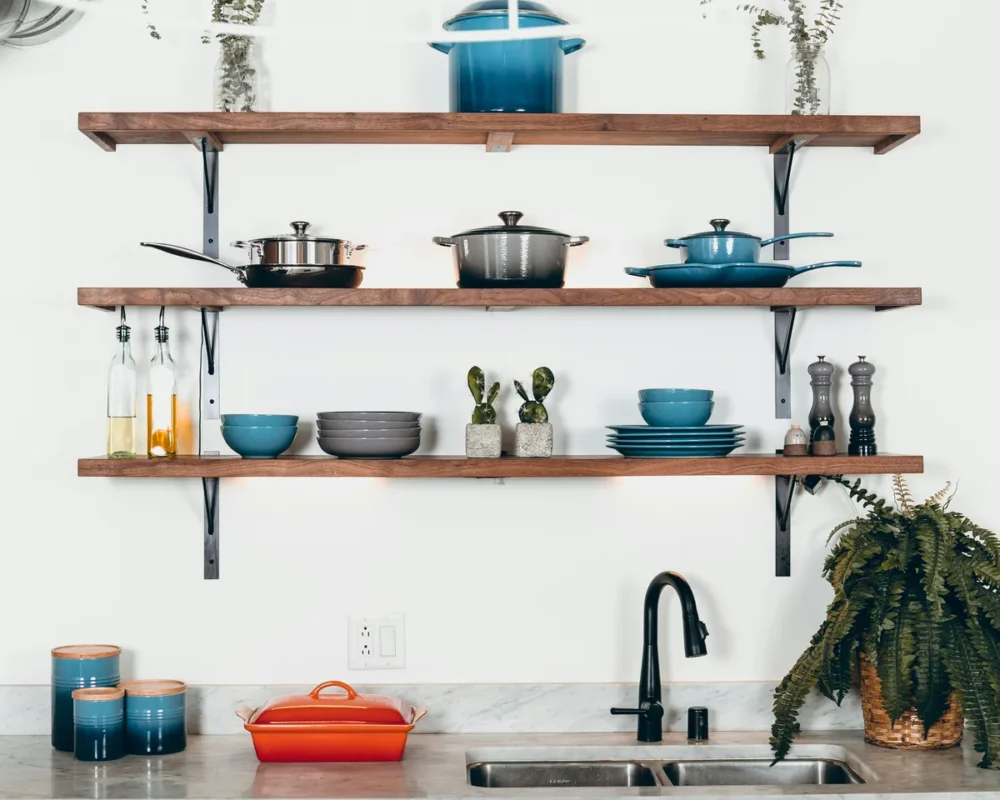 Wooden open kitchen shelves displaying pots pans stacked dishes and cacti