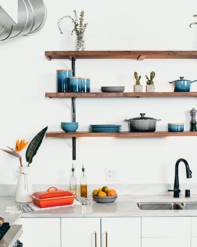Kitchen wall with open wooden shelves styled with blue canisters and plants