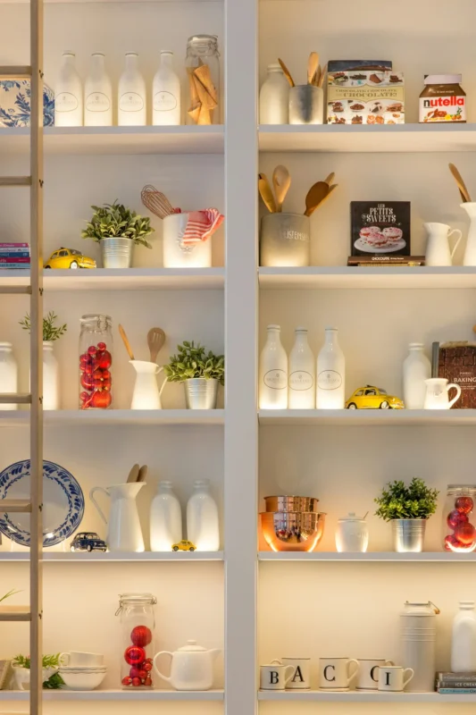 Organized pantry shelves with glass jars white bottles and cookbooks