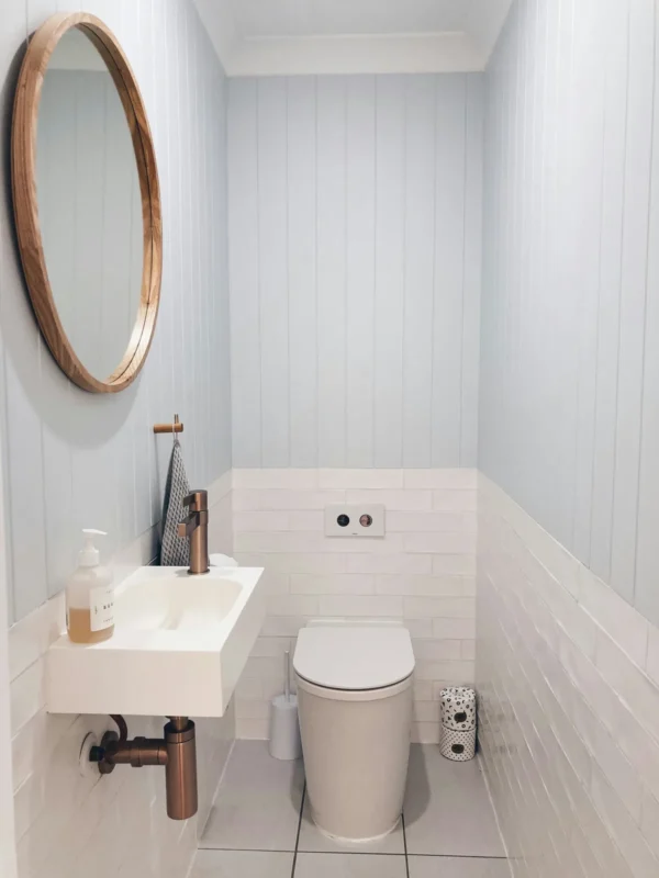 Tiny powder room with wall-hung sink round wooden mirror and blue panelled walls