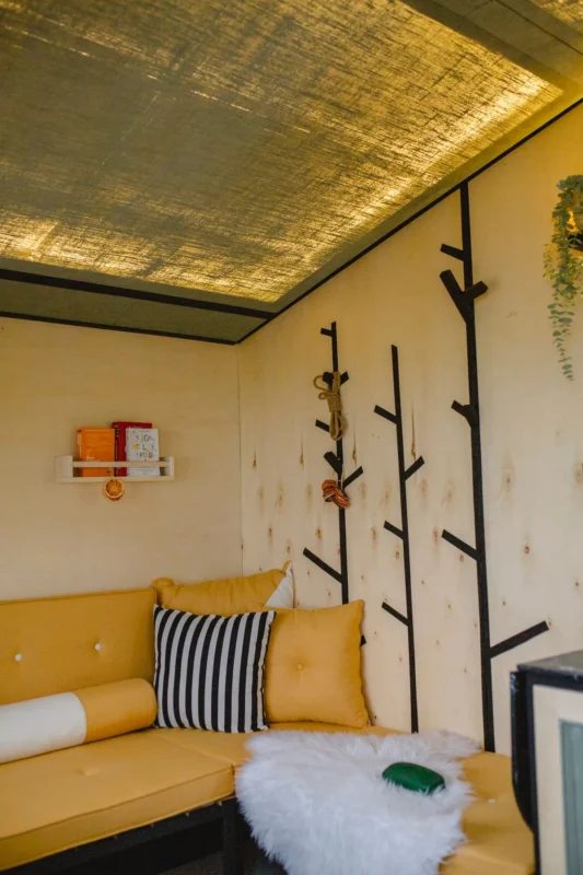 Tiny living room with mustard yellow sofa and tree branch wall hooks