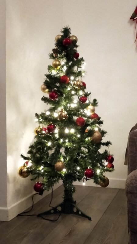 Slim decorated Christmas tree tucked into the corner of a small living room