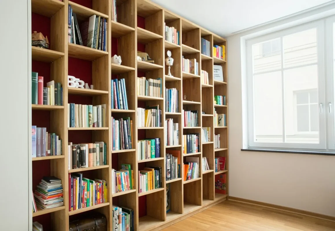 Floor-to-ceiling wooden bookshelf wall full of books beside a window
