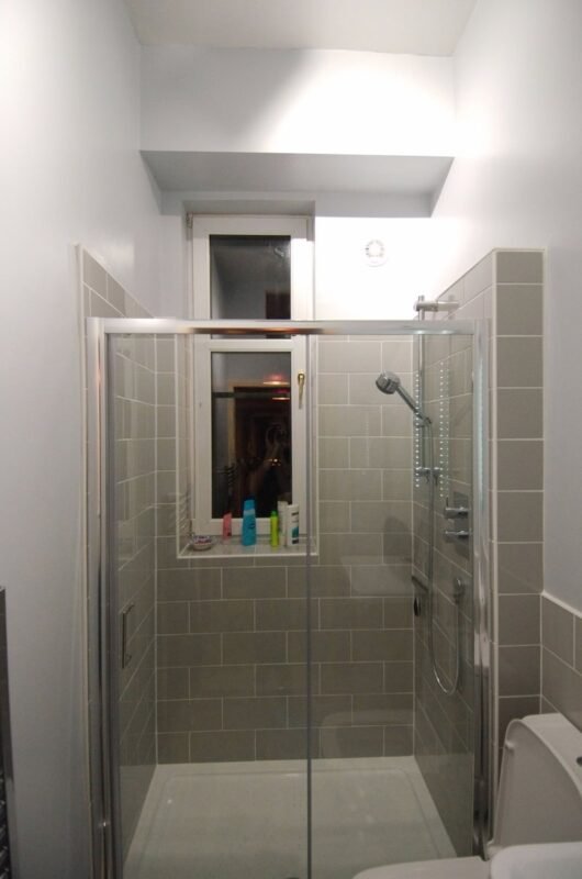 Glass shower enclosure with grey subway tile in a renovated small bathroom