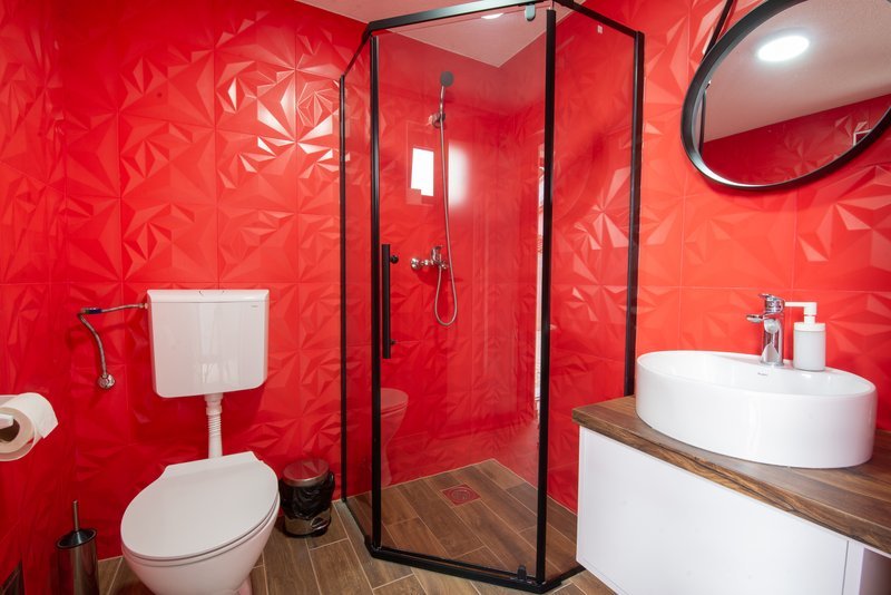 Bold red tiled small bathroom with corner shower enclosure and round mirror