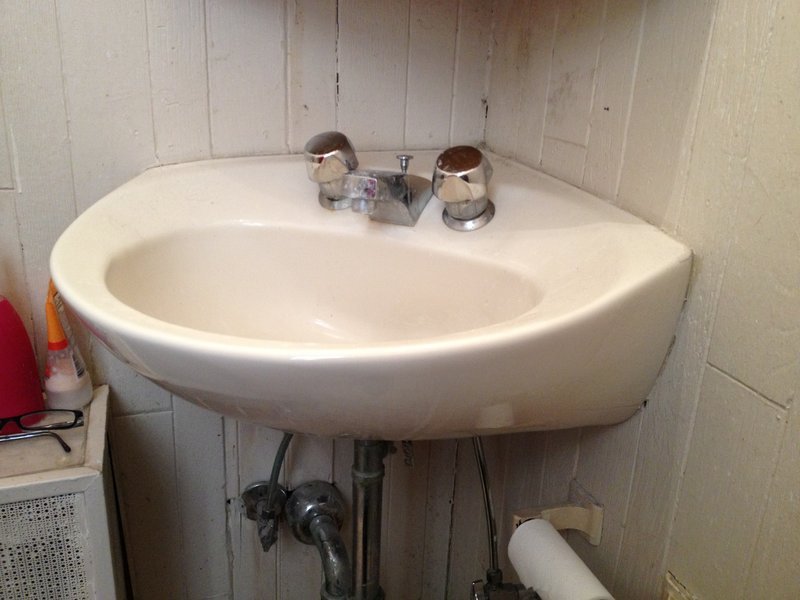 White corner sink mounted in a small bathroom to save floor space