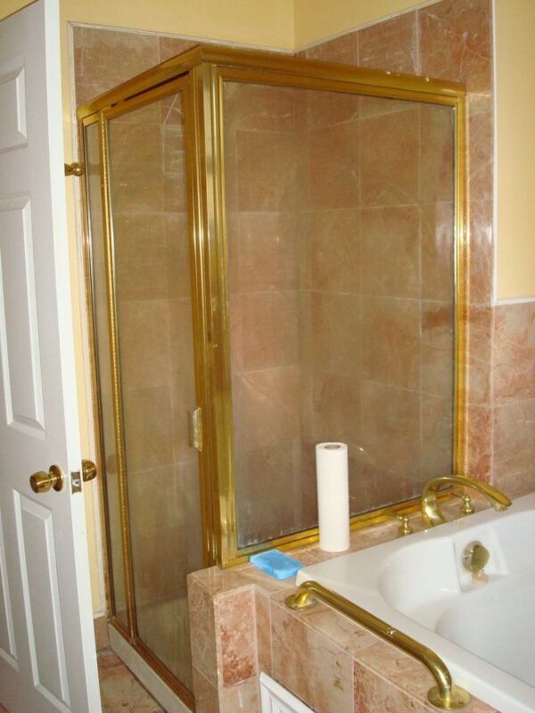 Brass-framed glass shower enclosure in a small tiled bathroom