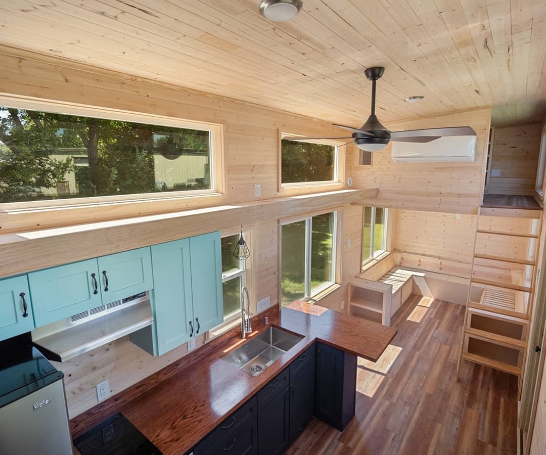 Bright tiny house kitchen with light wood cabinets, turquoise accents and loft ladder