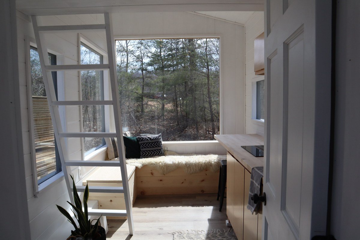 Bright white tiny house interior with window seat, ladder and forest view
