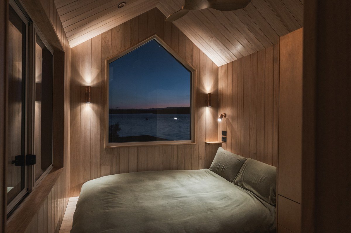 Tiny home bedroom at twilight with wood paneling and lake view through window, calm tiny living sleep space
