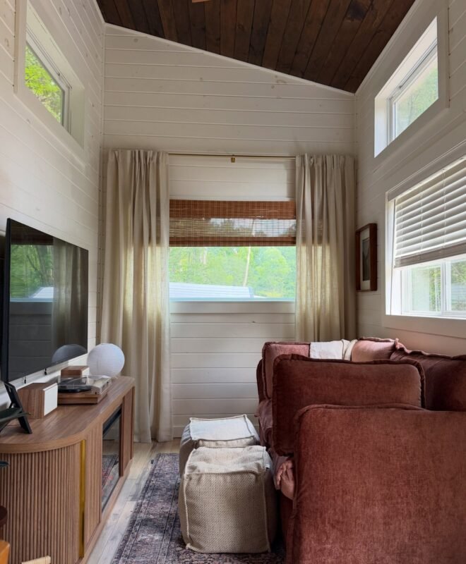Bright tiny home living room with white shiplap walls and big windows overlooking greenery