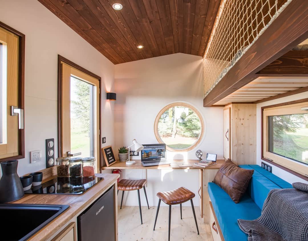 Compact tiny home workspace with round window, desk and blue sofa, calm work from home nook