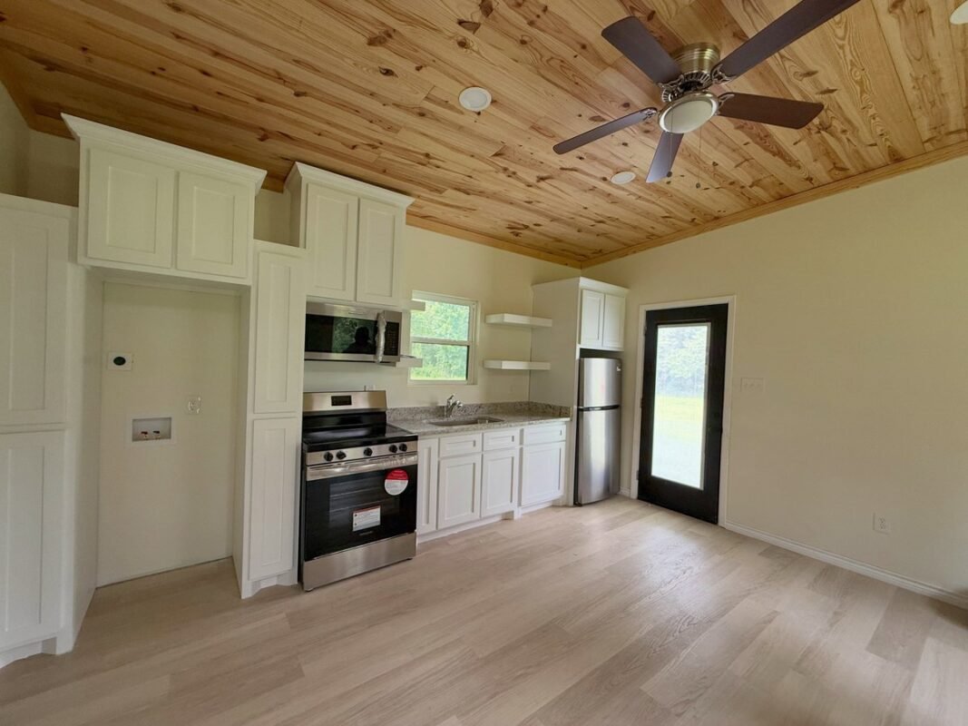 Compact tiny house kitchen with white shaker cabinets, stainless appliances, and wood plank ceiling